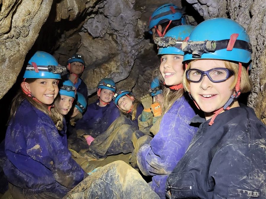 Smiling campers wearing helmets and headlamps inside a cave
