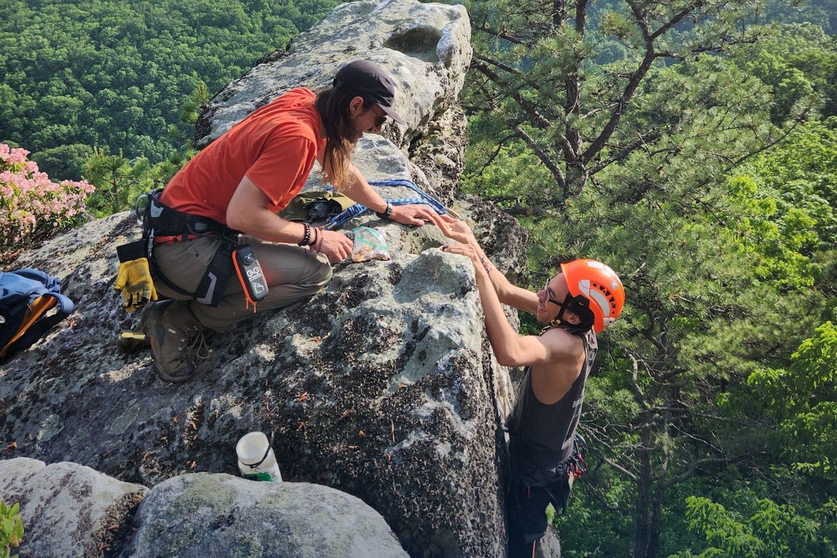 An instructor reaching down to help a climber up a rock face