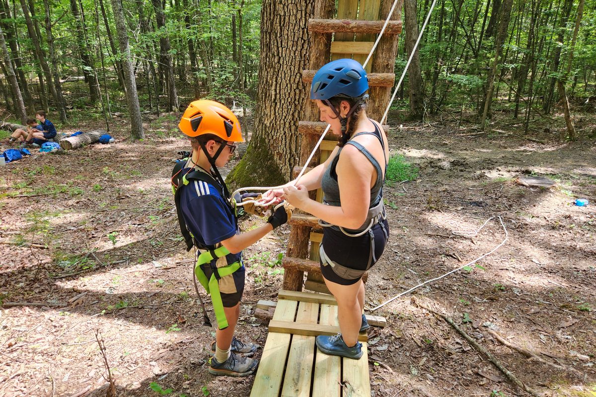 A counselor checking a young camper's harness at the ropes course