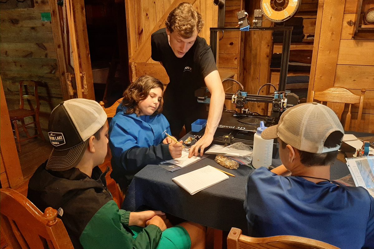 Campers learning to 3D print with a counselor at a table in the lodge