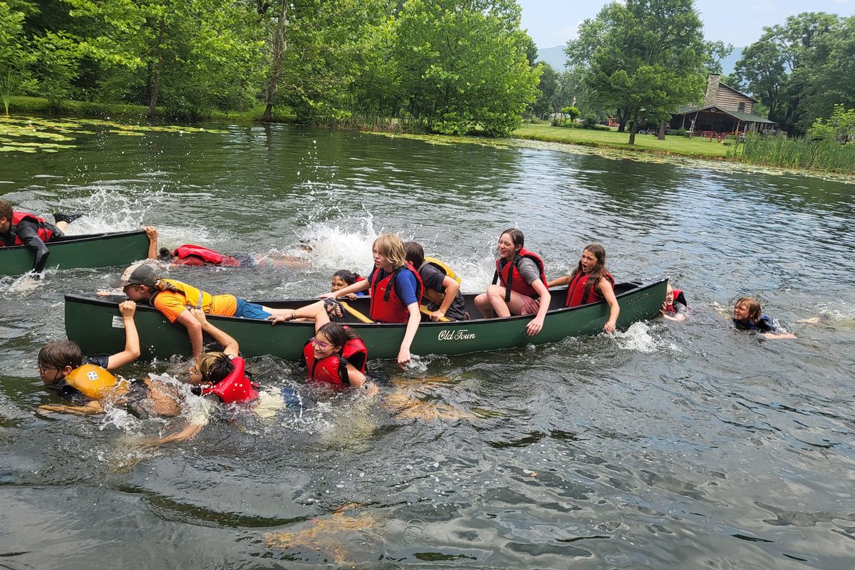 Campers tipping a canoe and swimming in the pond