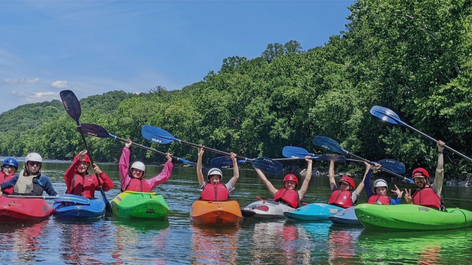 A line of campers in kayaks raising their paddles on the river