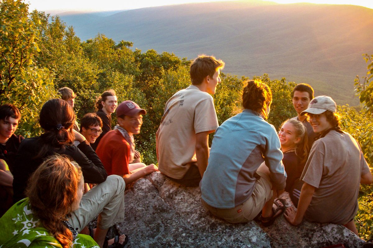 Older campers sitting together on a rock overlook at sunset