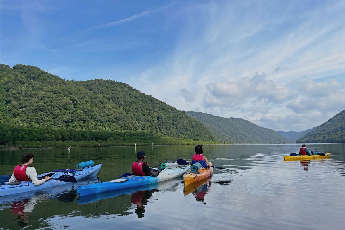 Campers paddling kayaks on a wide mountain river