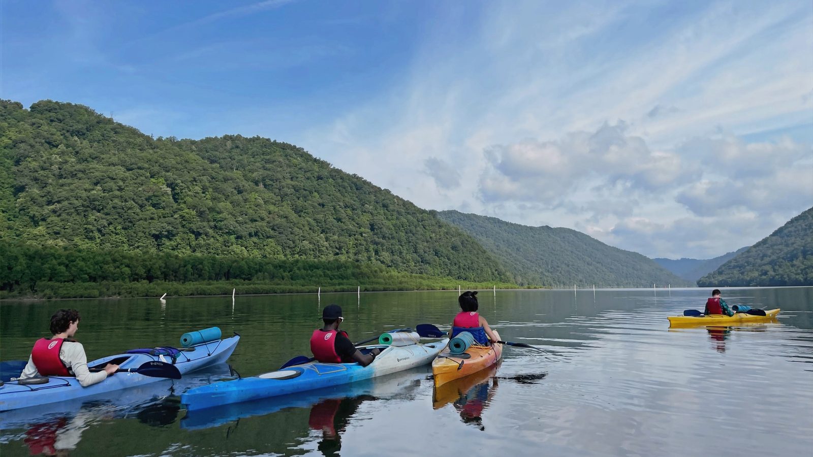 Campers paddling kayaks on a wide mountain river