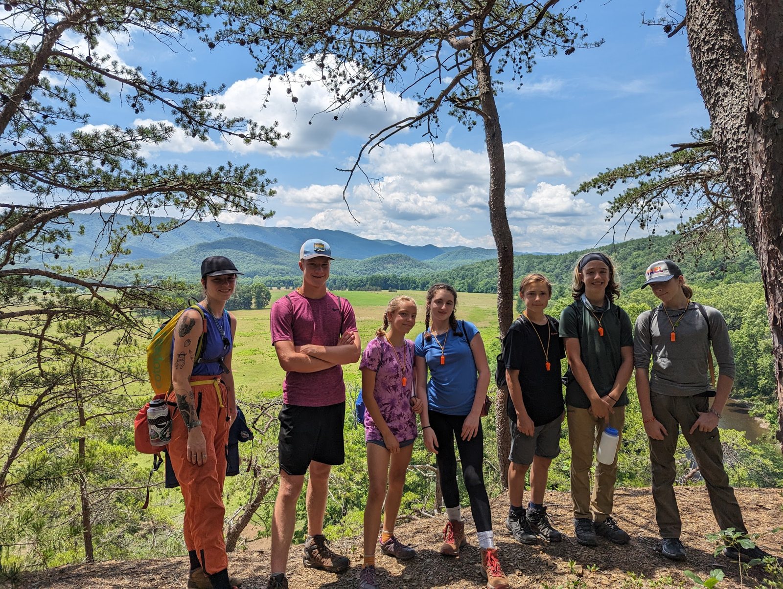 Campers and a counselor at a wooded overlook above a green mountain valley