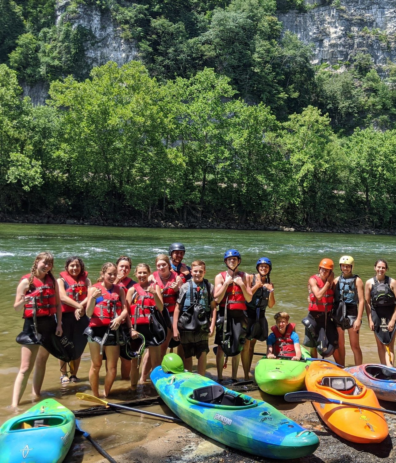 A group of campers in life jackets lined up with their kayaks at the river