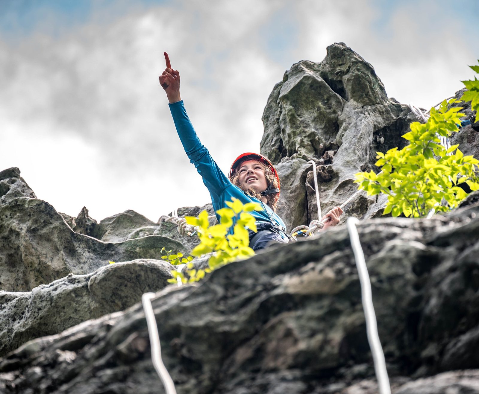 A climber in a red helmet cheering at the top of a rock climb