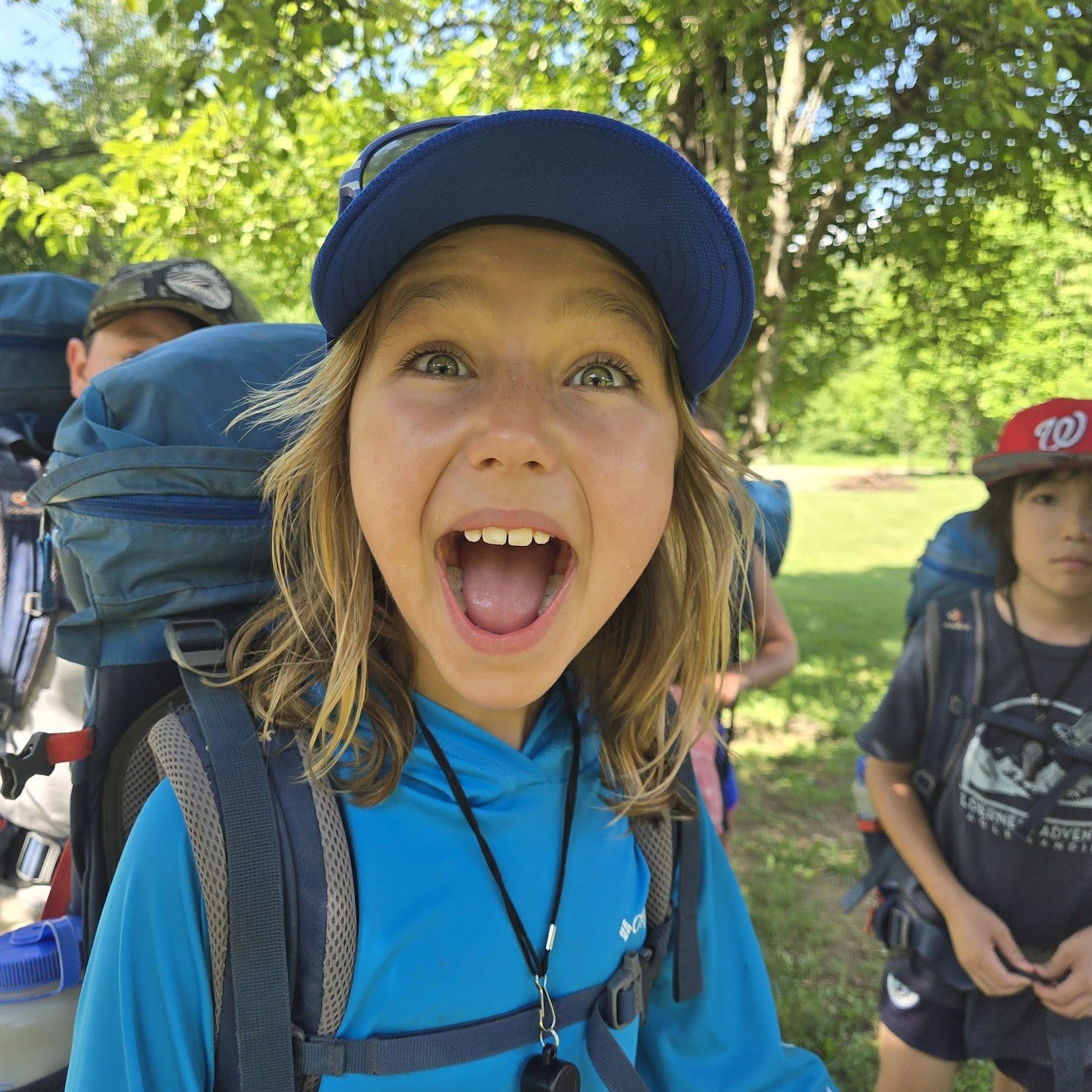 A grinning young camper in a cap and backpack