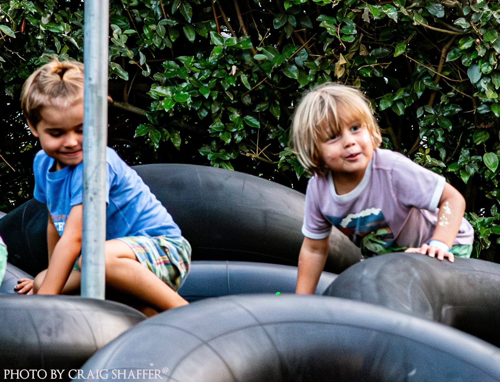 Two young children climbing on a pile of black inner tubes