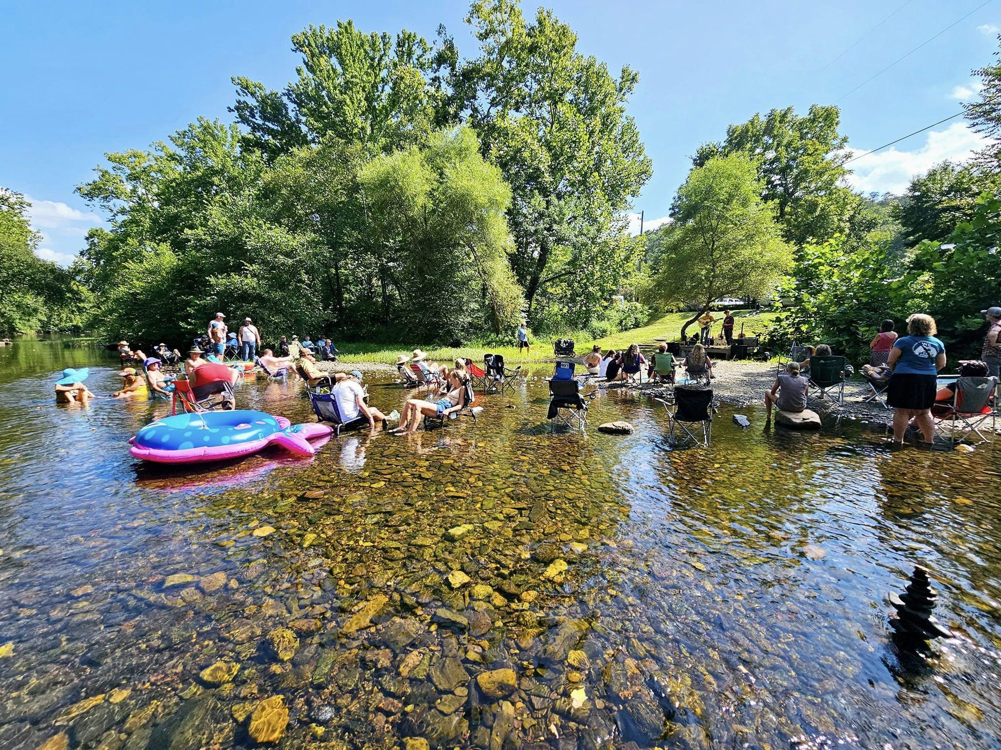 People floating on tubes and wading in a clear, shallow creek on a sunny day
