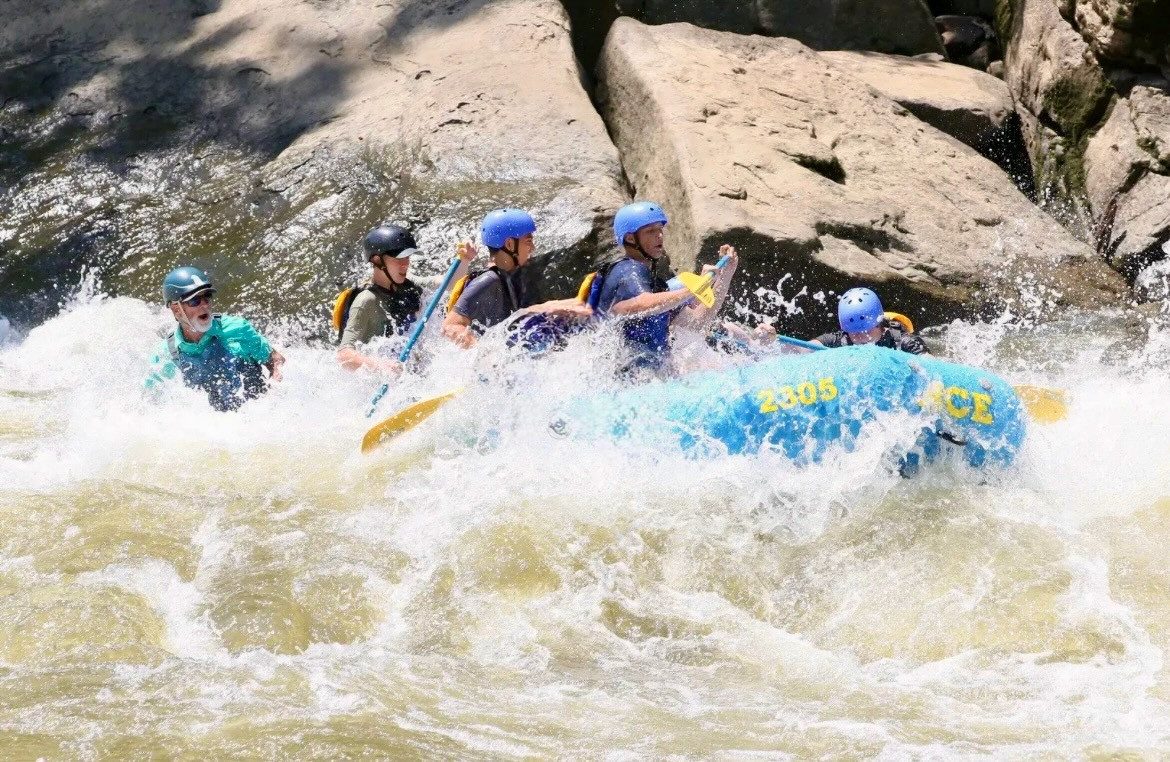 Campers in helmets paddling a raft through whitewater with a guide