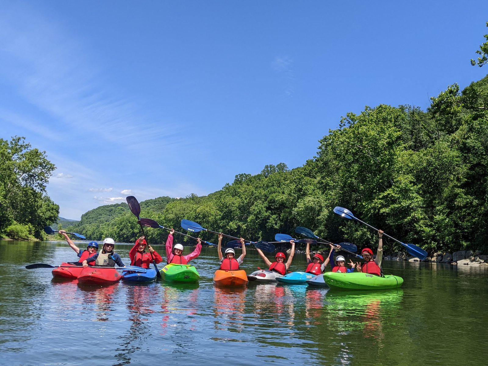 A line of campers in kayaks raising their paddles on the river