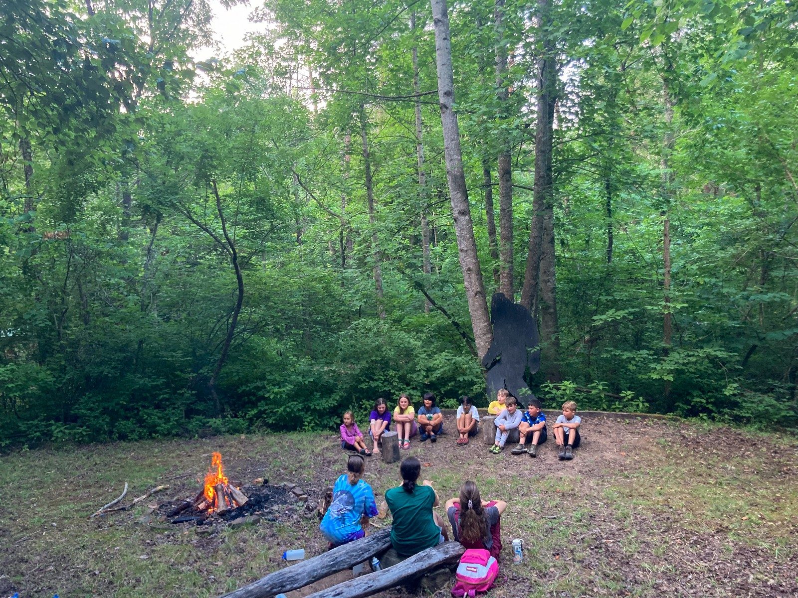 Campers sitting around a small campfire in a forest clearing