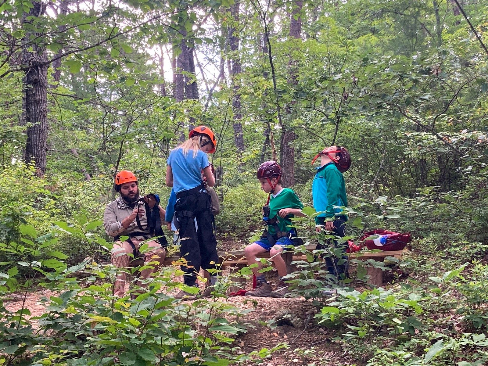Campers in helmets putting on harnesses in the woods