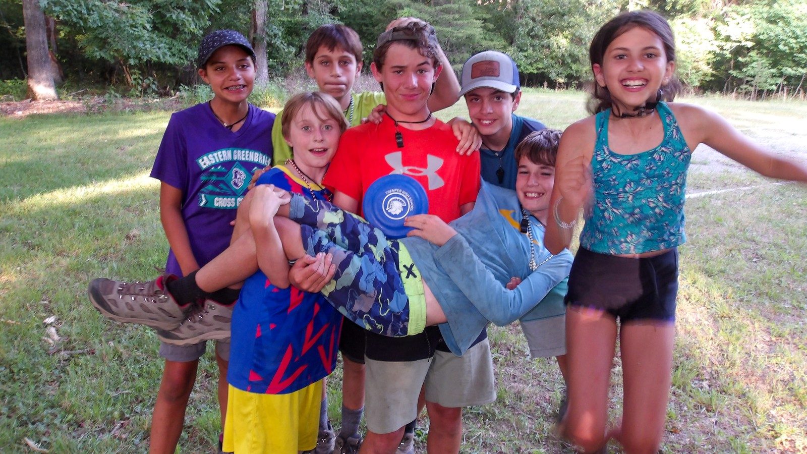 Grinning campers holding a friend up for a group photo on the field