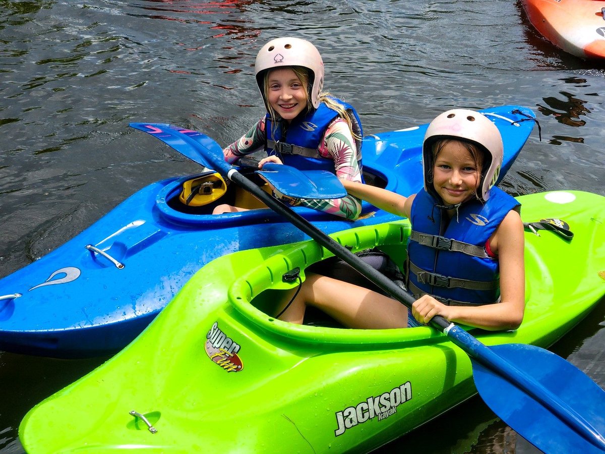 Two smiling campers in helmets sitting in their kayaks on the pond