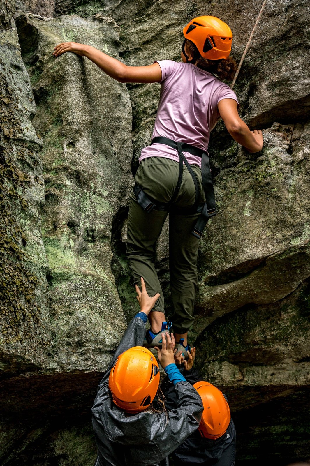 Helmeted campers supporting a climber on a rock face