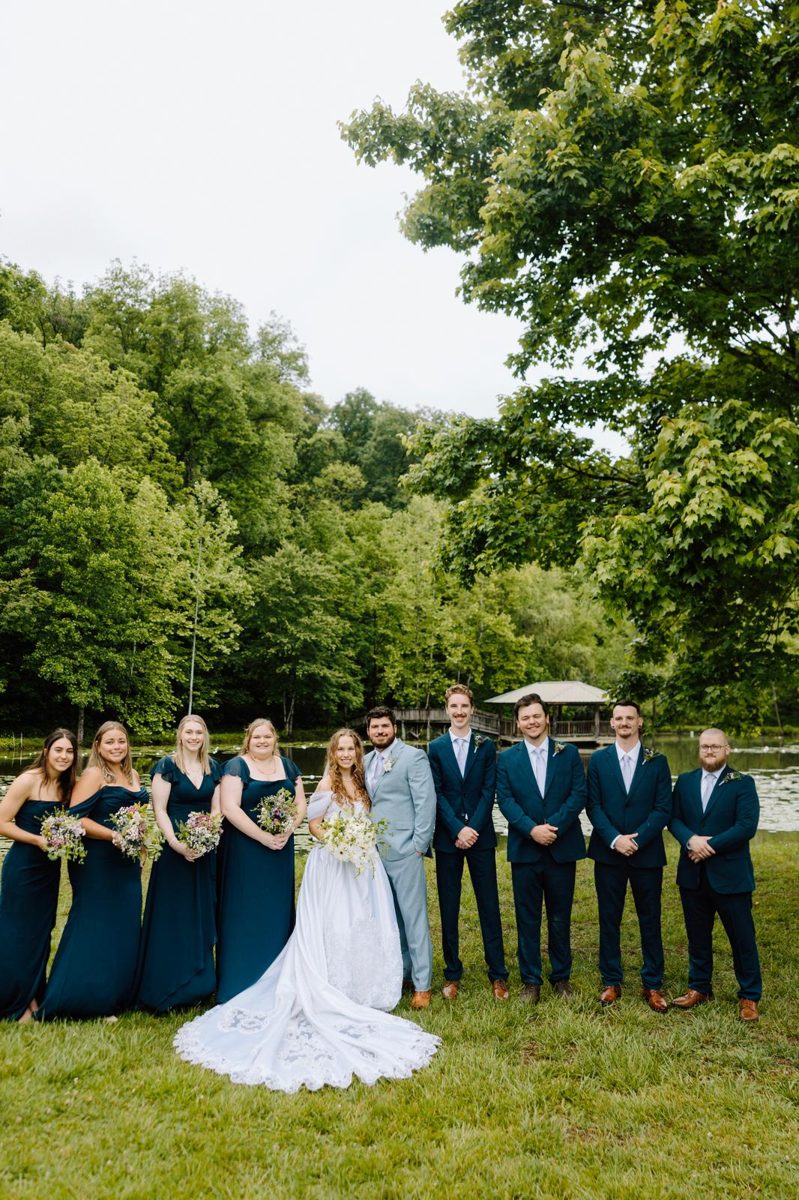 A wedding party gathered on the lawn beneath leafy trees