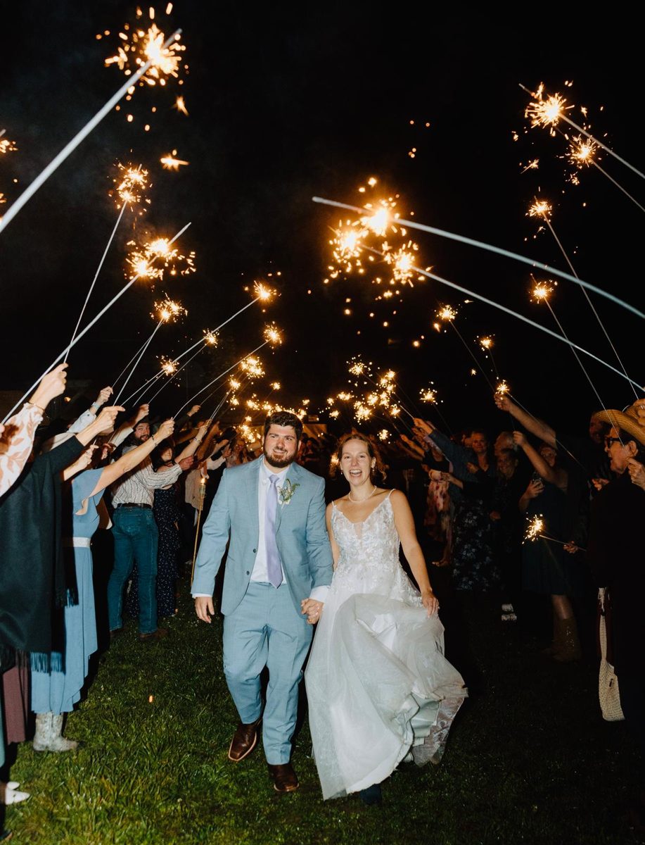 A wedding couple walking between guests holding sparklers at night