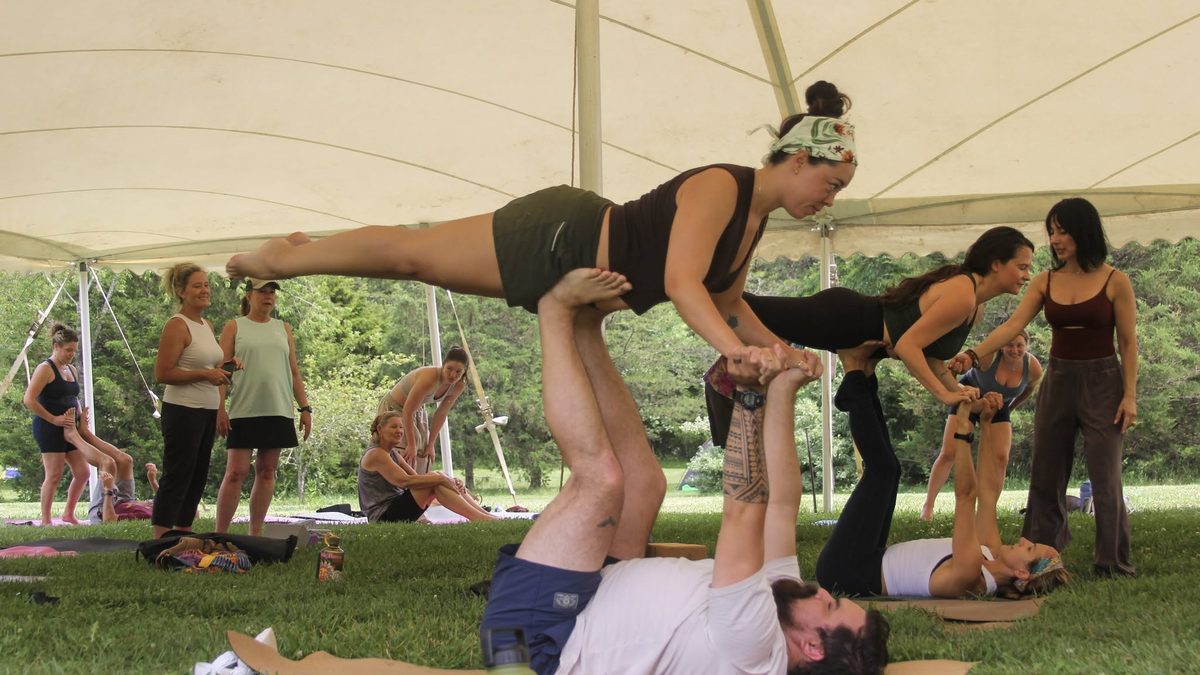 Participants practicing partner acrobatics under a tent at Yoga Venture